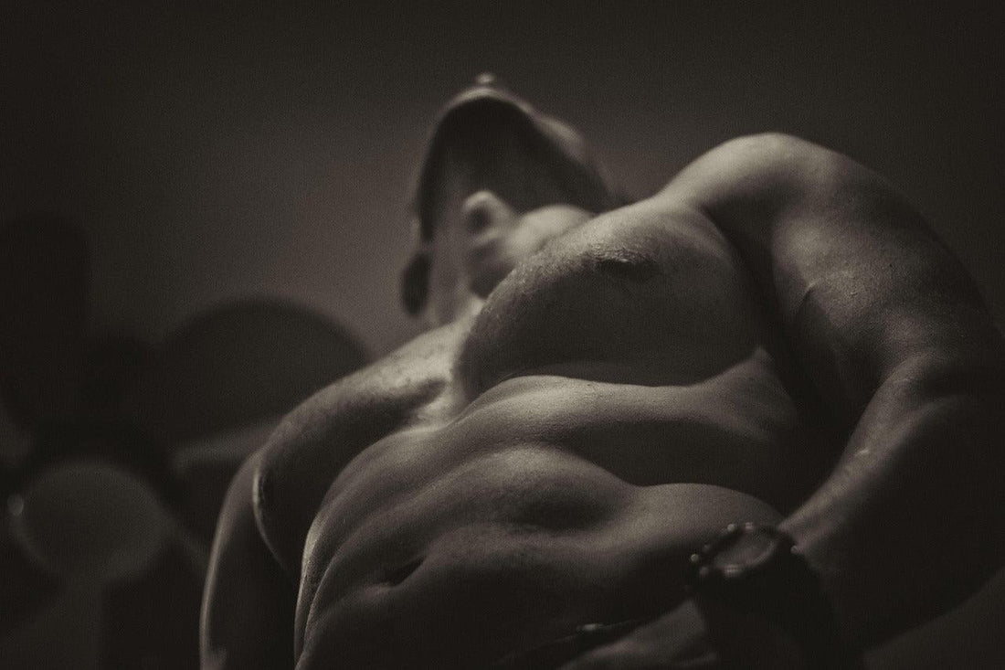 Black and white close-up of muscular male torso and abs in dim light