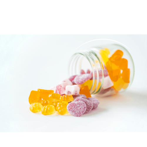 Glass jar tipped over with orange and purple gummy candies spilled on white surface