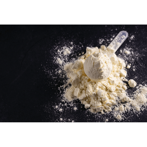 Scoop of white protein powder on black surface, spilled powder around scoop