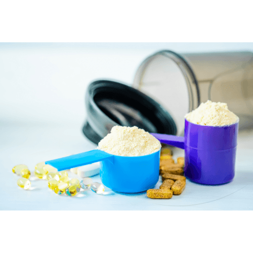 Blue and purple scoops of protein powder with yellow capsules and vitamin tablets next to a black-lid container